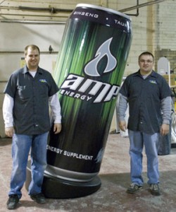 Travis Cantwell (left) and Todd Randall of Elite Signs & Graphix stand next to the 7-foot tall Amp can, the trademark energy drink of Pepsi Co., that they helped Signs By Benchmark produce for the 2009 ISA show.